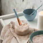zapalona świeca i miseczki z produktami do domowego spa